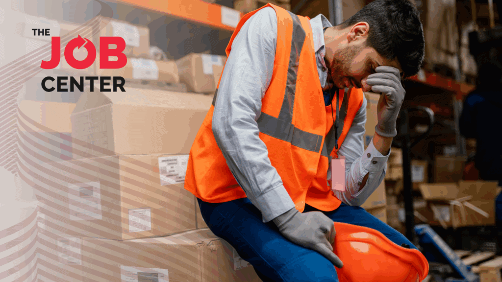 Overwhelmed warehouse worker sits on packaging boxes with head in hand